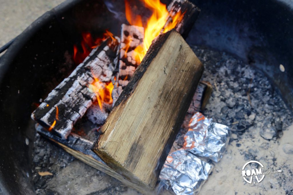 Apple crisp wrapped in foil packets baking in the fire pit by the log.