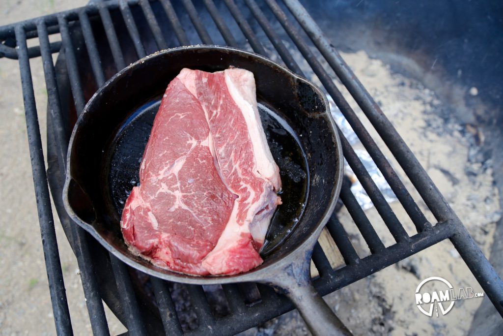 Steak in a heated cast iron pan over the fire.