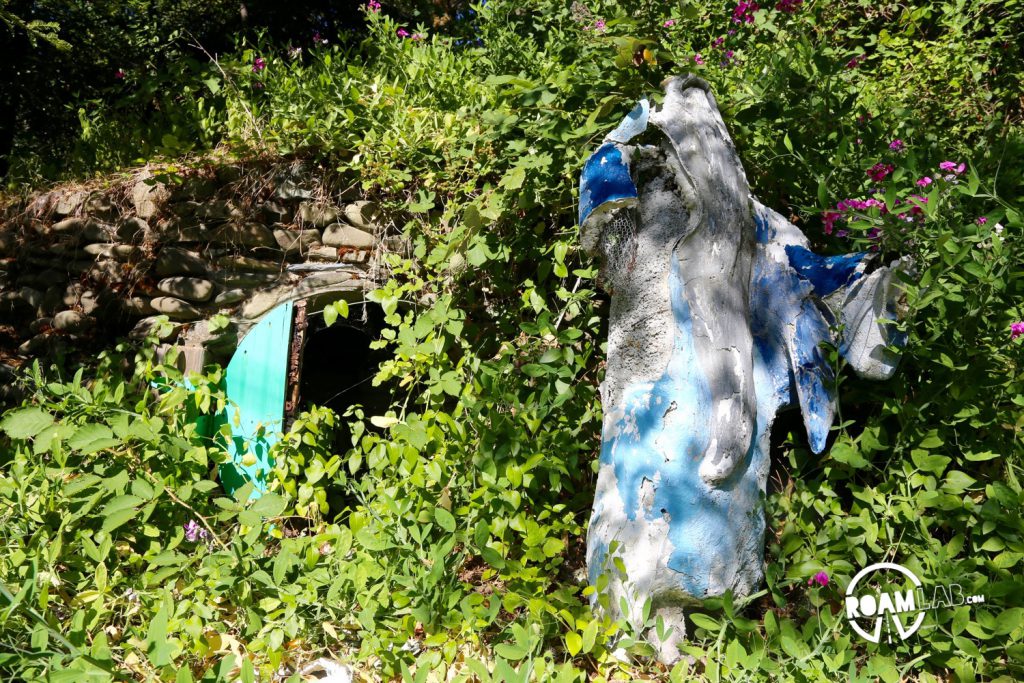 A partially decapitated statue of Gandalf the Grey teeters next to the green doors of Bilbo Baggins's hobbit hole.