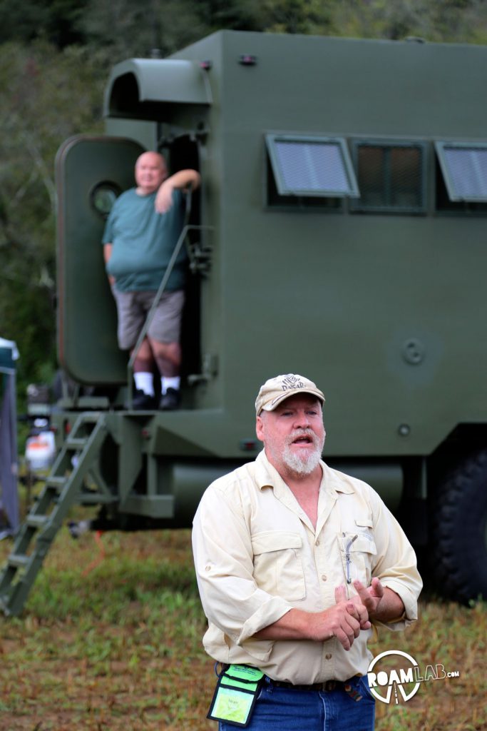 A presenter at the Overland Expo East 2016 discusses custom made motor homes with examples ranging between jeeps, ambulances, and the massive military vehicle in the background of this picture.