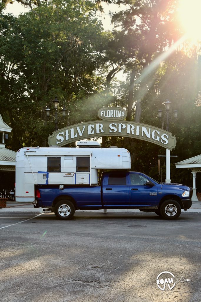 Sun shining down on a 1970 Avion C11 truck camper parked outside the entry to Silver Springs State Park, Florida.