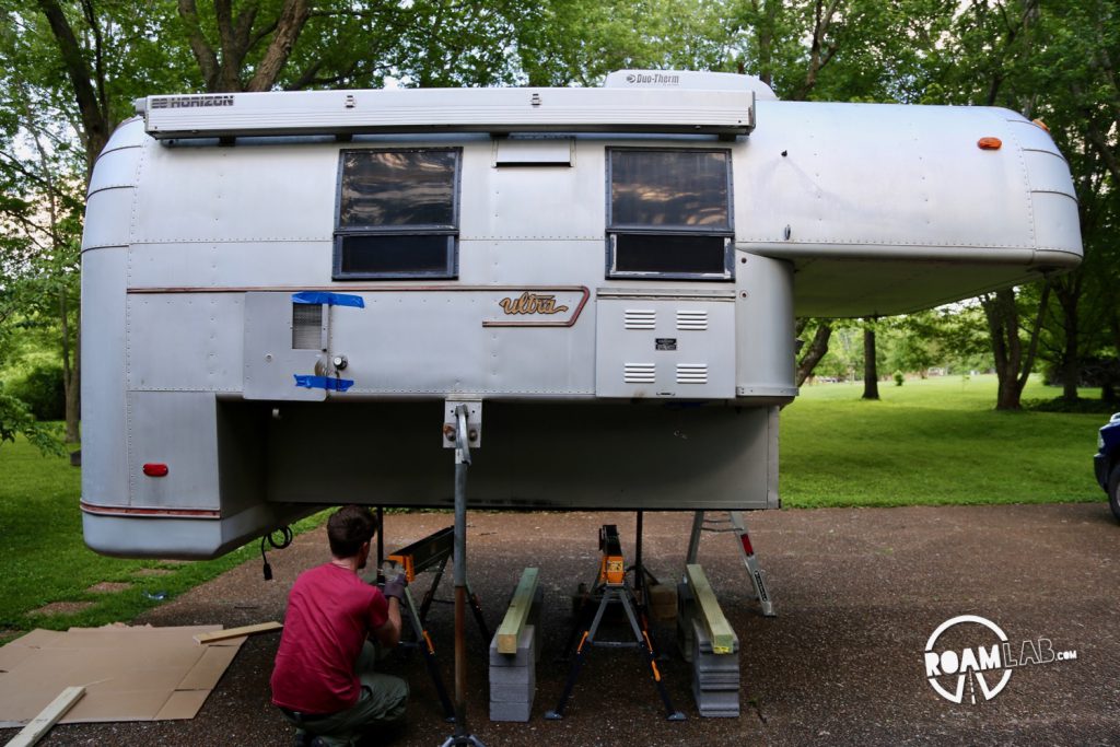 Man arranging cinder blocks and 4x4 lumber to support a 1970 Avion C11 truck camper on jacks.