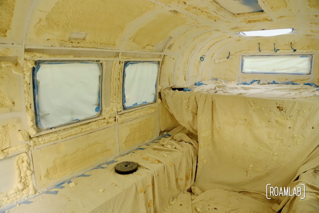 Truck camper interior covered with drop clothes, plastic sheet, and masking tape after painting.