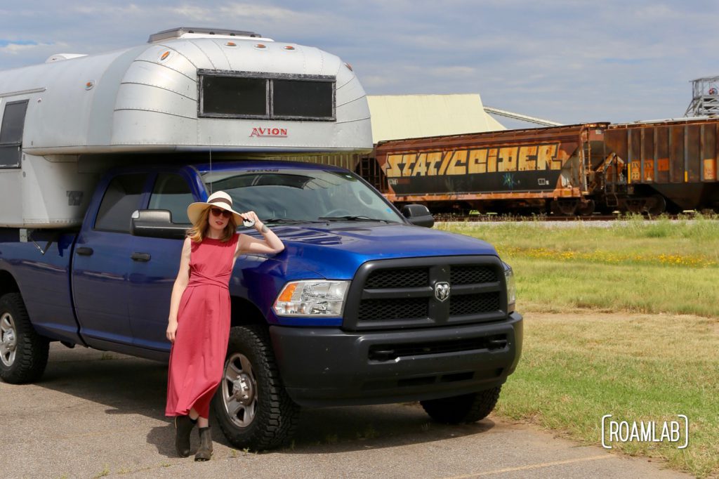 Woman next to a 1970 Avion C11 truck camper by the train tracks