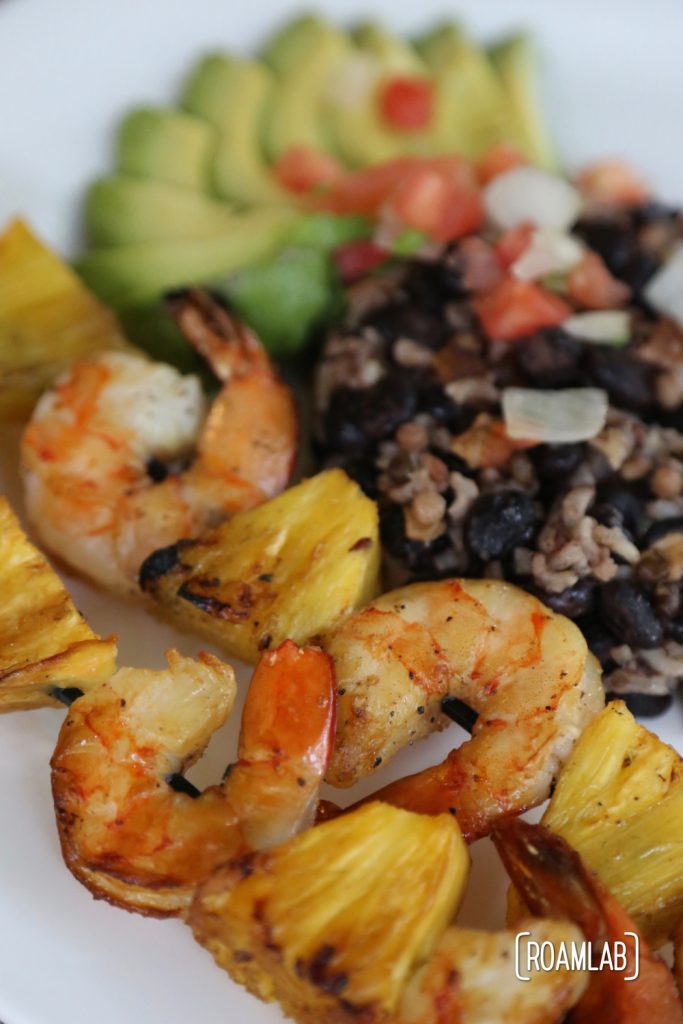 Pineapple shrimp skewers with avocado, beans, rice, and pico de gallo.