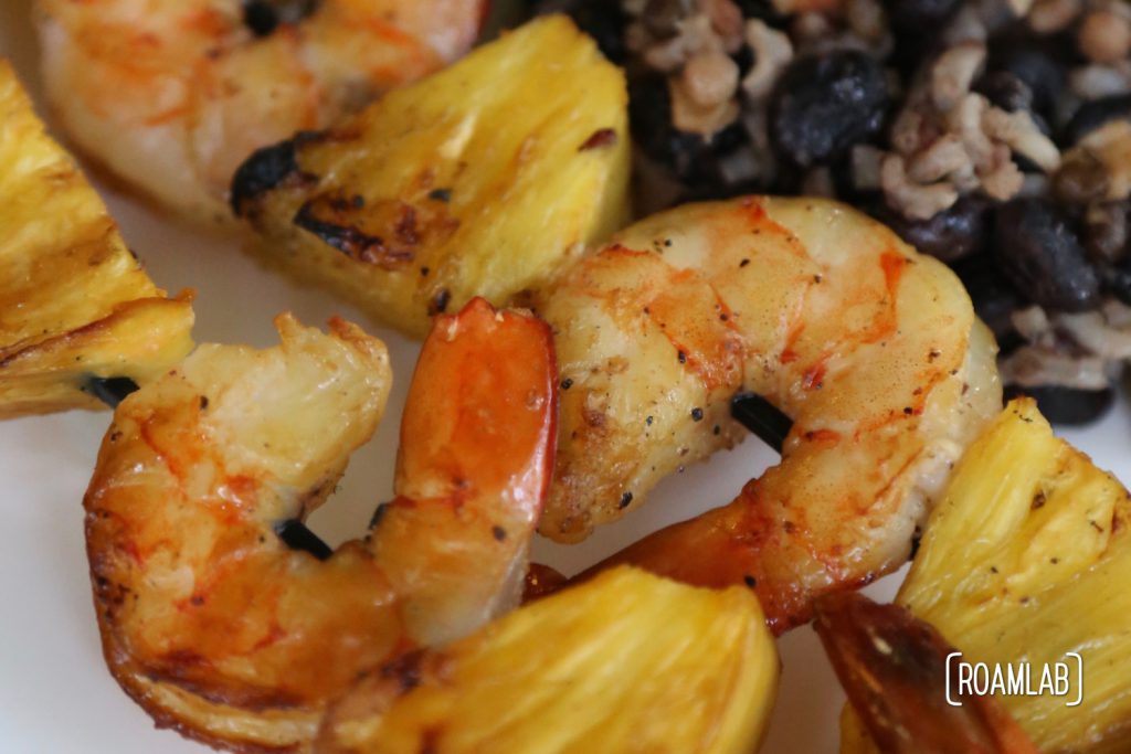 Pineapple shrimp skewers with avocado, beans, rice, and pico de gallo.