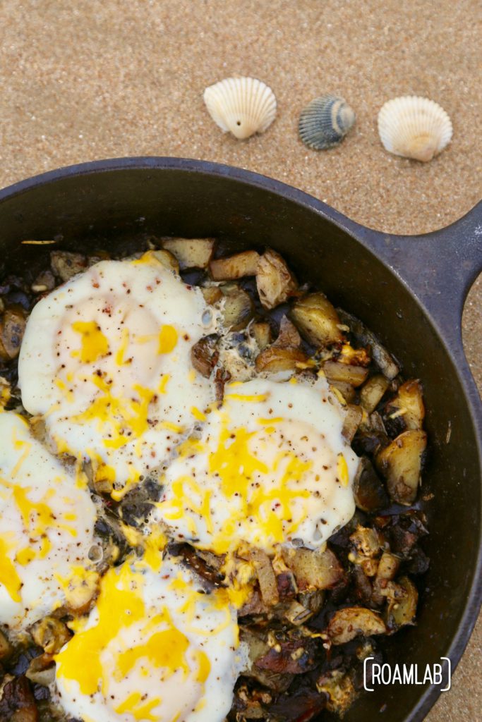 Cast iron skillet bacon and eggs hash on the beach.
