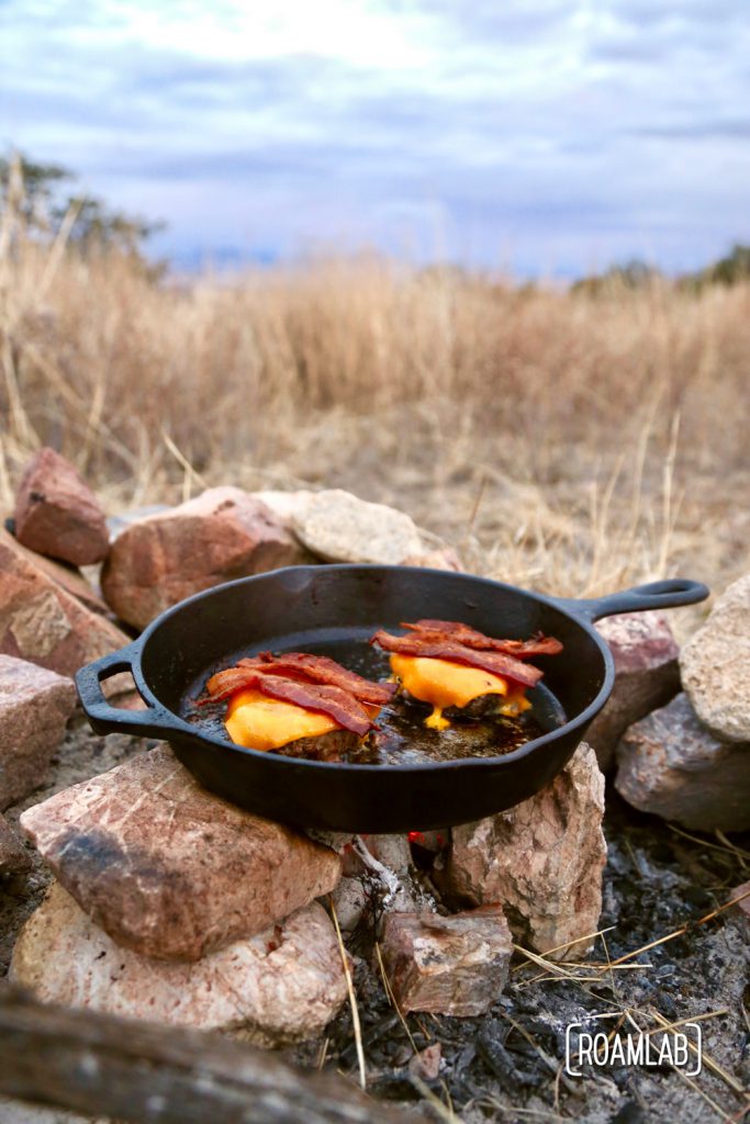 Bacon cheddar cheeseburger on a skillet over the coals.