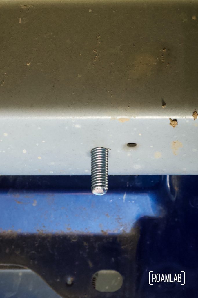 Bolt in place through frame brace as seen from under the truck bed.  The grey bar is part of the truck frame.