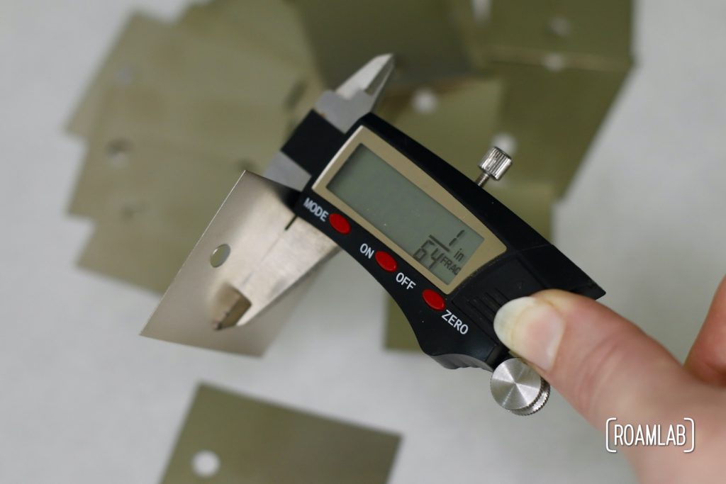 Using digital calipers to measure the thickenss of sheet metal bus bars.  The display reads 1/64 inch.