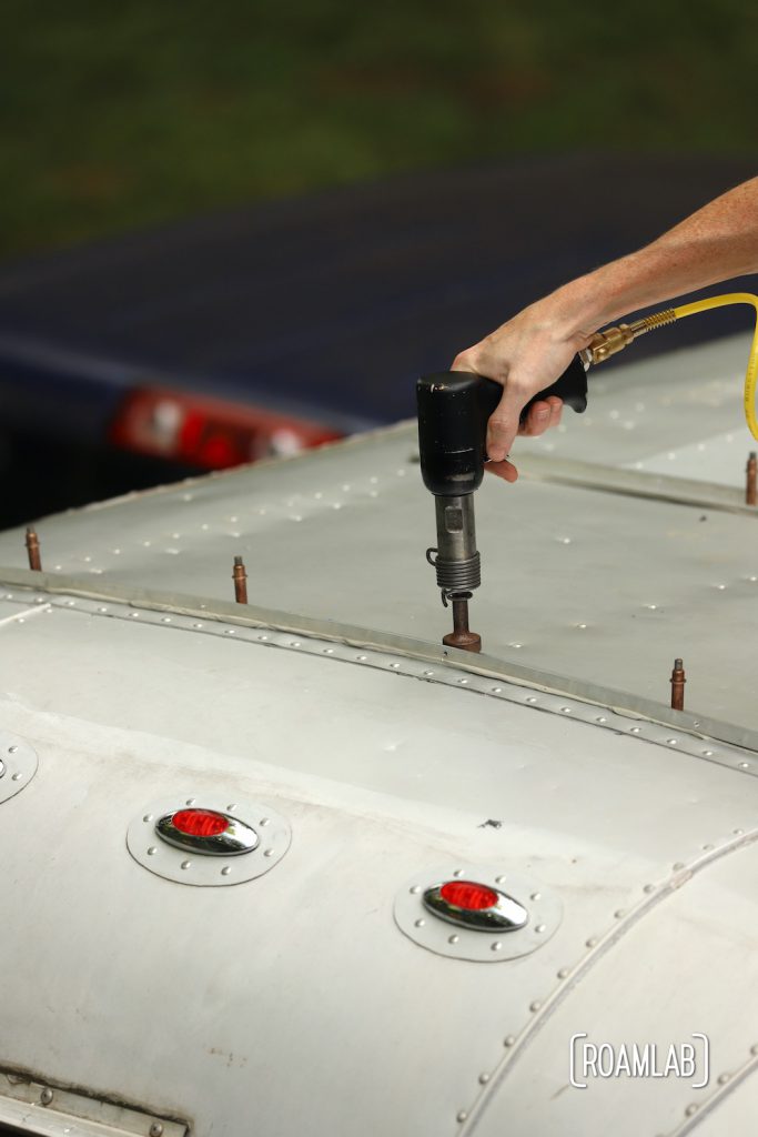 Hand holding a rivet gun to the roof of the aluminum 1970 Avion C11 truck camper.