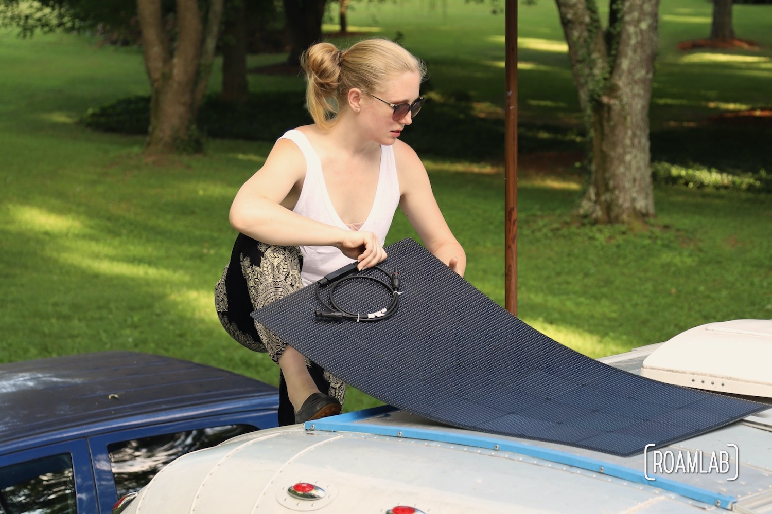 Woman placing a flexible solar panel on an aluminum camper roof.