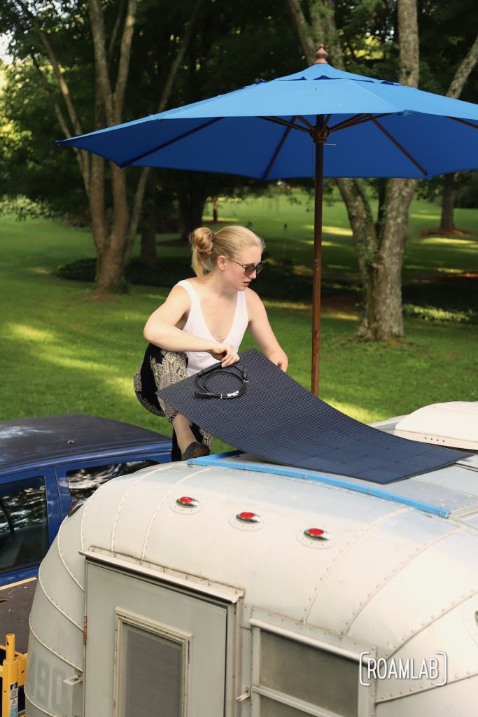 Woman holding a solar panel against the roof of a 1970 Avion C11 truck camper.