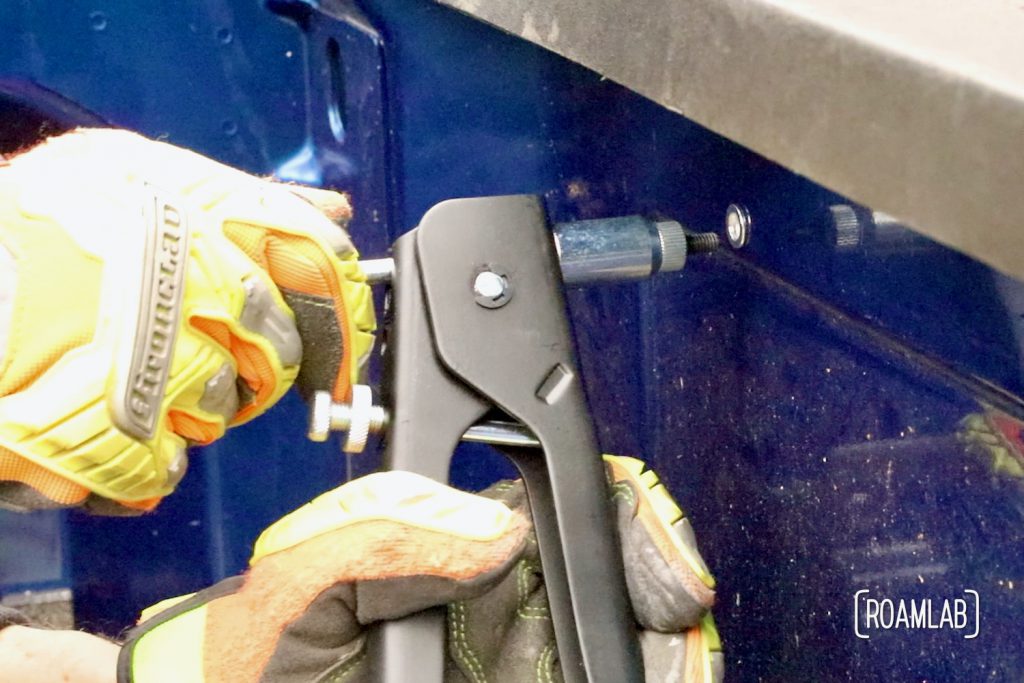 Using a rivet gun to install a rivet nut into the side of a blue truck bed.