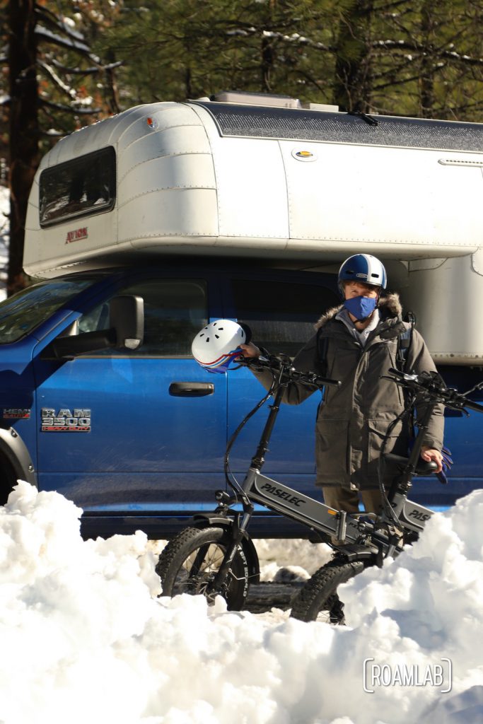 Man holding out bicycle helmet while standing by two bikes and a 1970 Avion C11 truck camper.