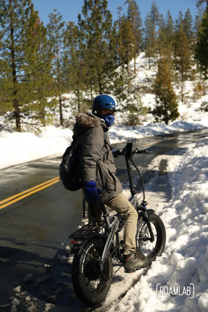 Man on a bike on the side of a road flanked by thick snow and pine trees in the Foresthill OHV Trail System