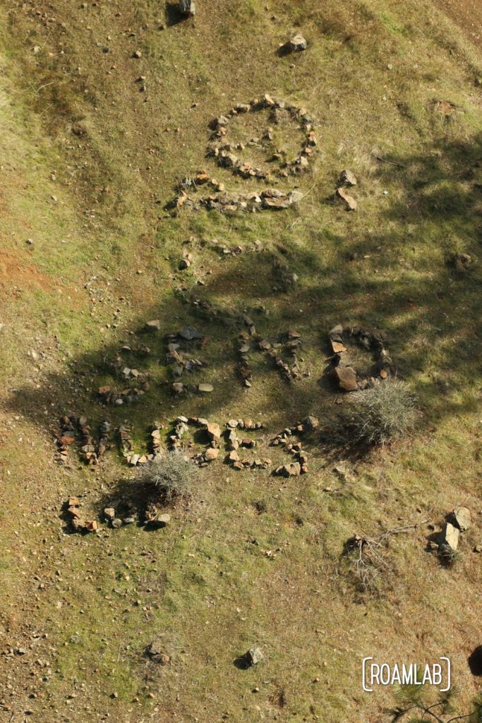 Rocks arranged on the ground to spell "SEND NUDES" from the air.
