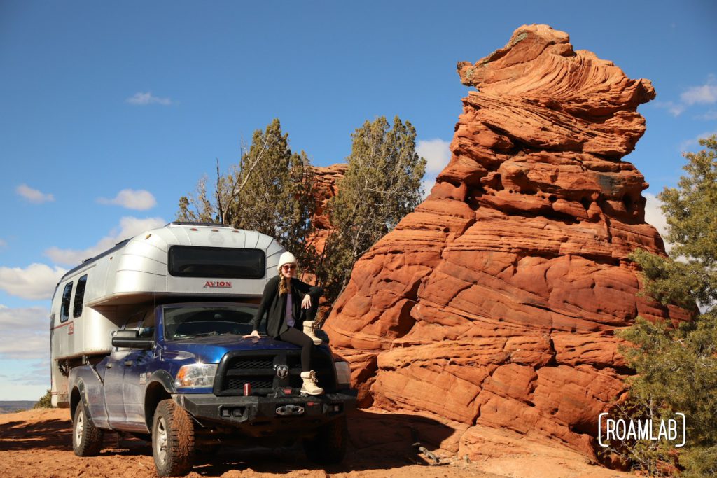 Woman sitting on a 1970 Avion C11 truck camper parked next to a red rock hoodoo in Vermillion Hills National Monument.