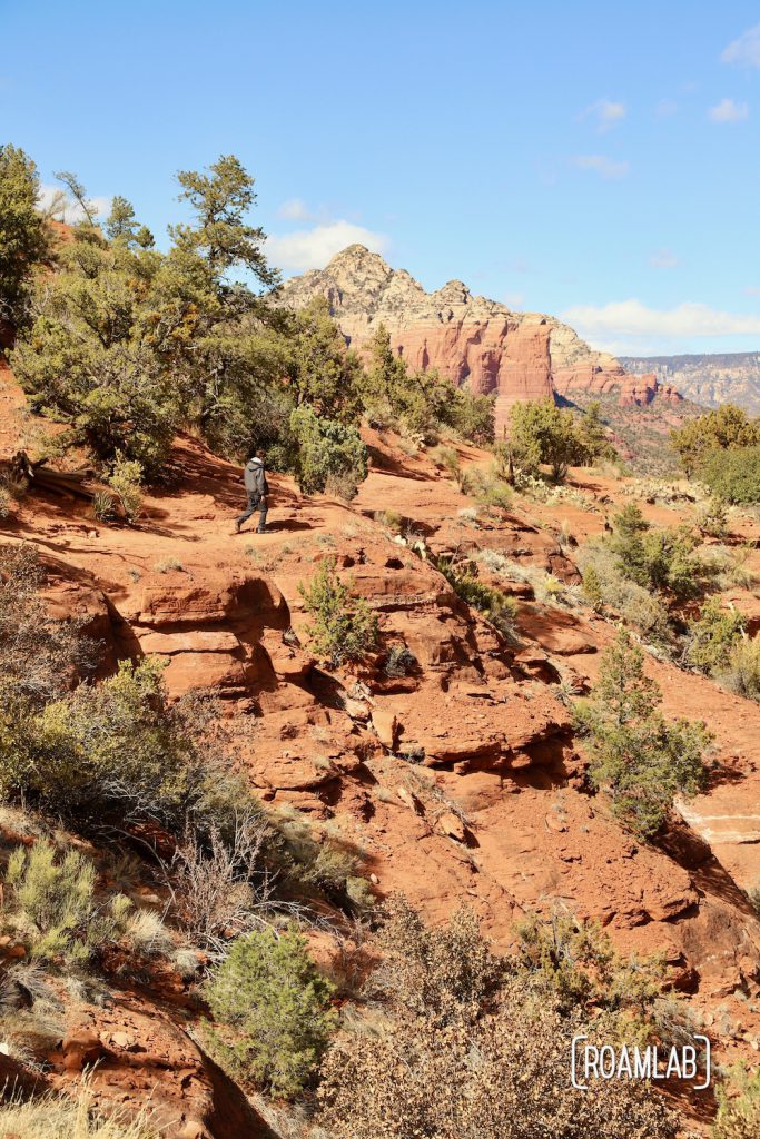 Man hiking along a red rock shelf on Airport Loop Trail in Sedona, Arizona.