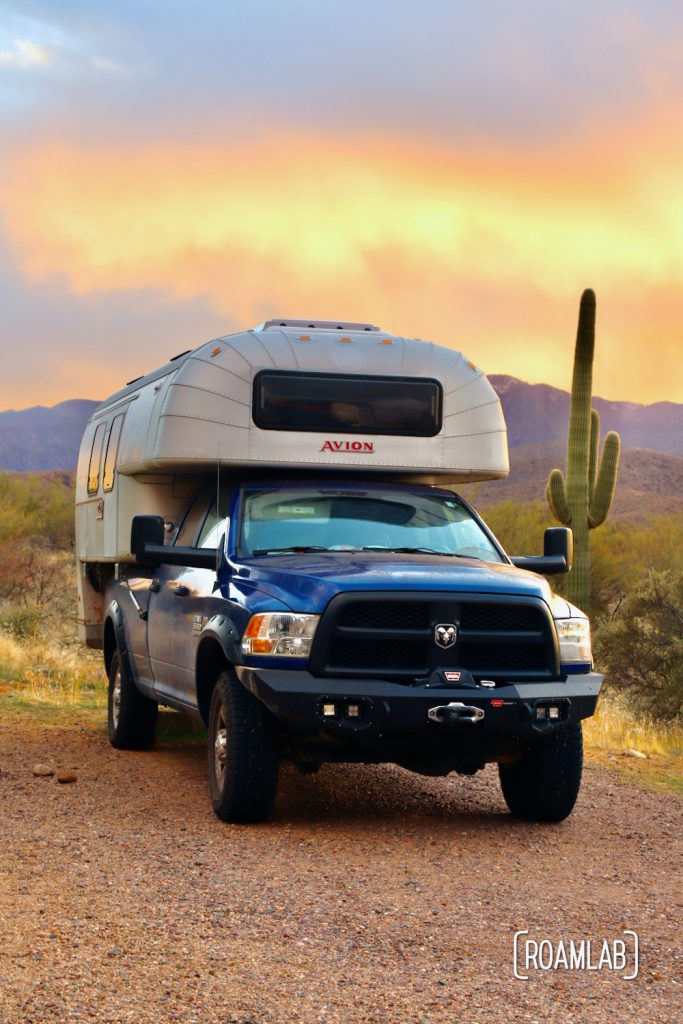 A brilliant sunset lighting up the background with a 1970 Avion C11 truck camper parked at Cholla Campground.