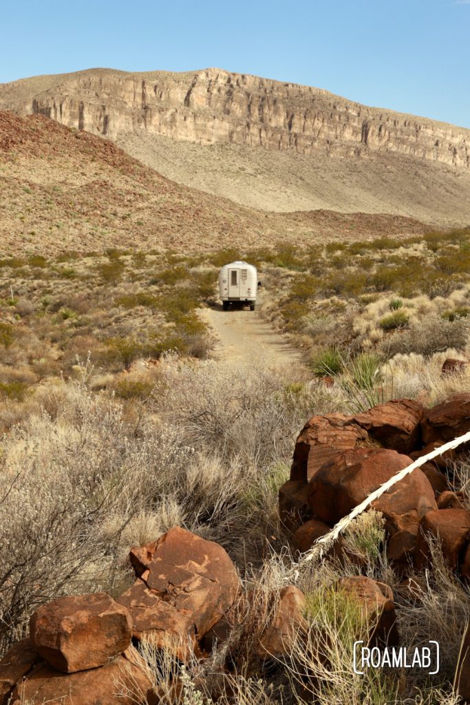 Dusty 1970 Avion C11 truck camper driving down a single land dirt road approaching the dramatic cliffs of the Alto Relex paralleling Old Ore Road in Big Bend National Park, Texas. 