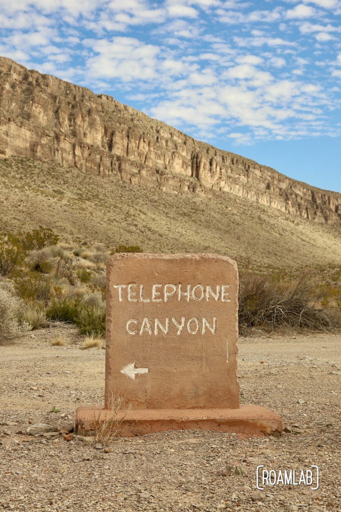 Grave stone like road marker for the Telephone Canyon Access Road off of Old Ore Road with cliffs and blue sky in the background.