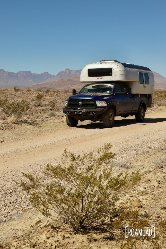 1970 Avion C11 truck camper driving down a wide flat dirt trail, River Road, in Big Bend National Parl.