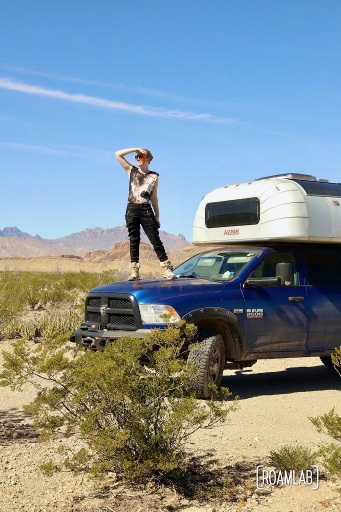 Woman standing on the hood of a 1970 Avion C11 truck camper parked at Fresno Campsite off River Road in Big Bend National Park, Texas.