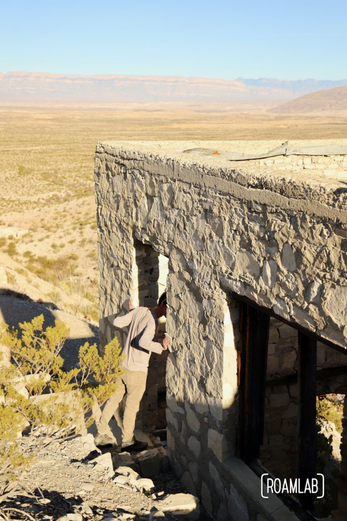 Man looking into a grey stone building with a desert spread out below.