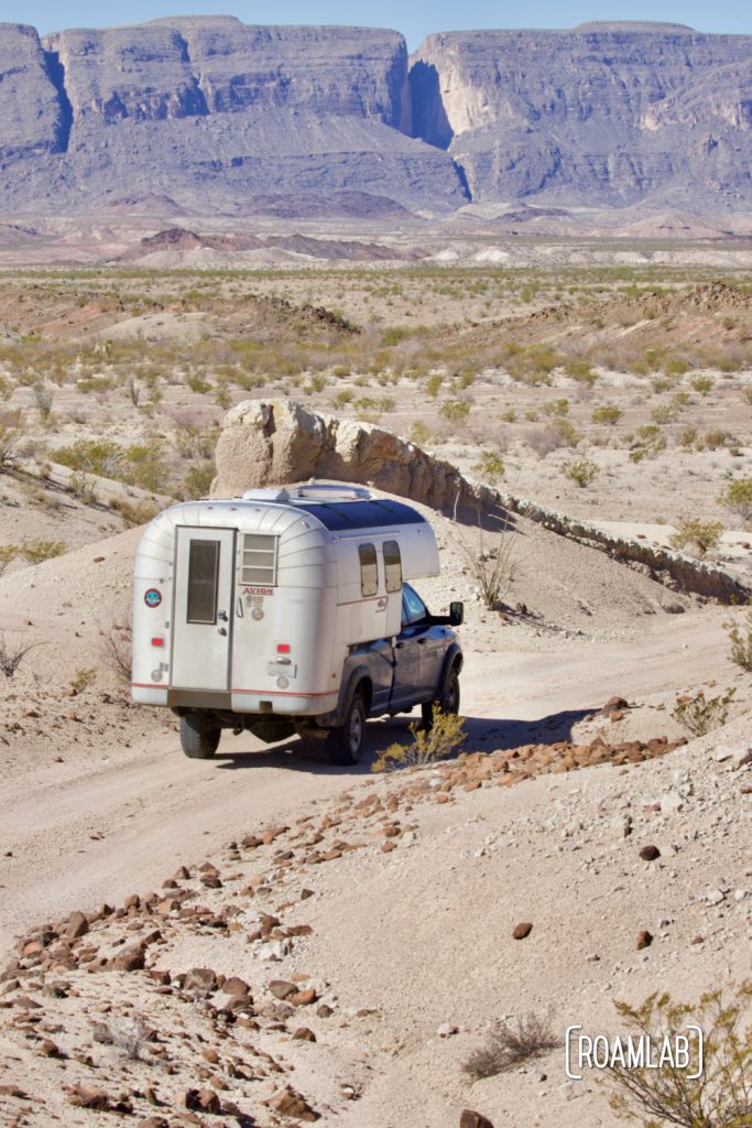 Vintage 1970 Avion C11 truck camper driving down a dirt road with purple mountains in the background along River Road in Big Bend National Park, Texas