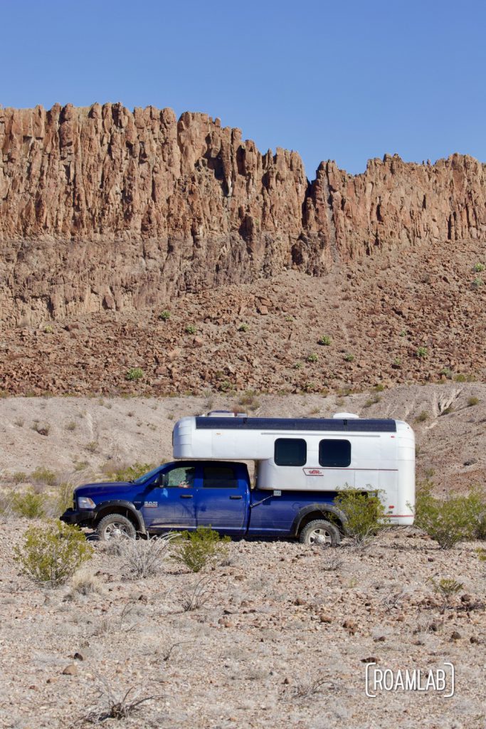 Aluminum 1970 Avion C11 truck camper with a rock face in the background driving down River Road in Big Bend National Park, Texas.