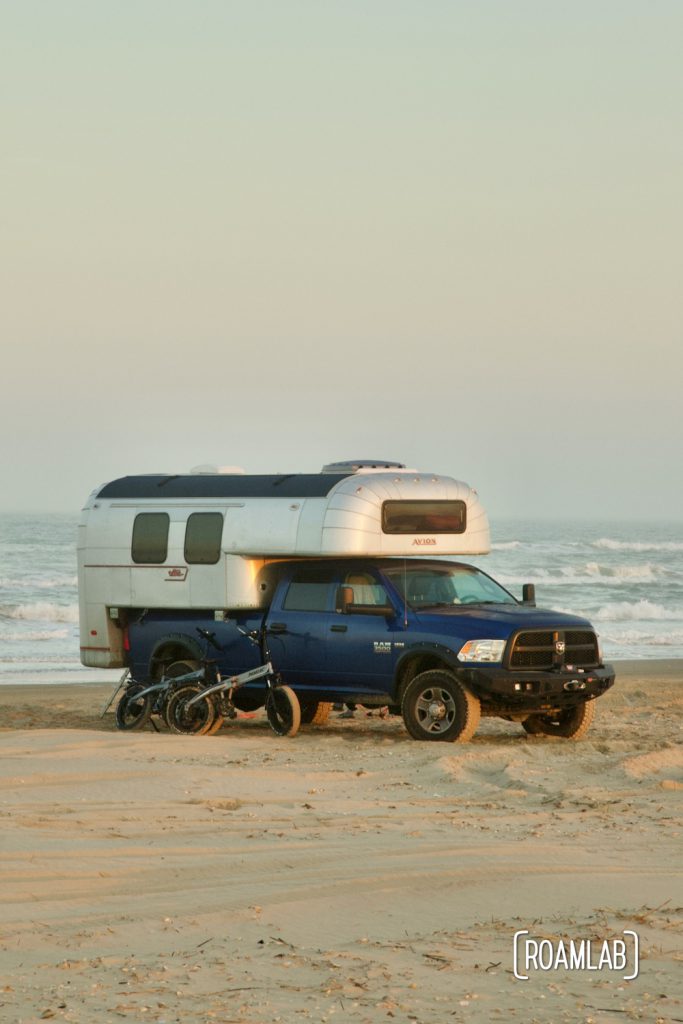 Two bicycles leaning up against a 1970 Avion C11 truck camper at dusk on the beach in South Padre Island, Texas.