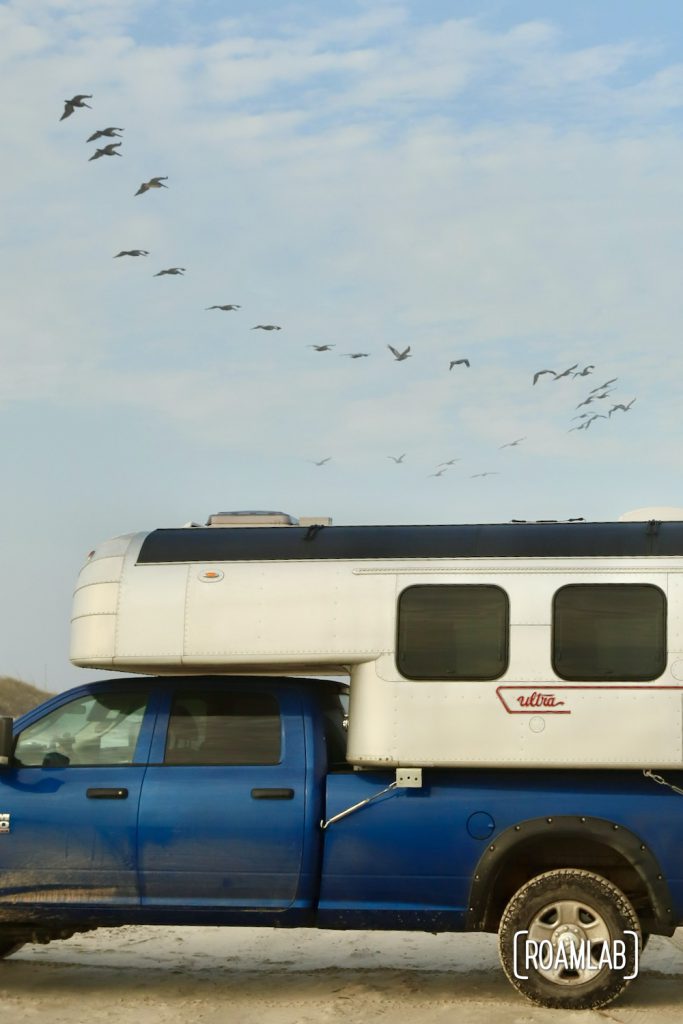 Pelicans flying over a 1970 Avion C11 truck camper parked on the beach at South Beach Padre Island National Seashore, Texas.