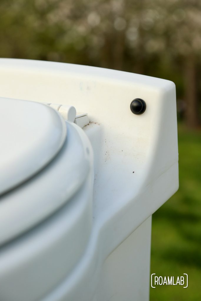 Closeup of a black button on the back panel of the Laveo By Dry Flush toilet.