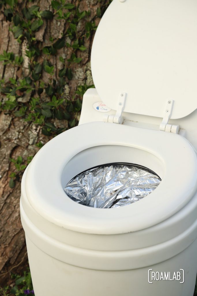 Laveo By Dry Flush toilet with cartridge installed, sitting in front of an ivy covered tree.