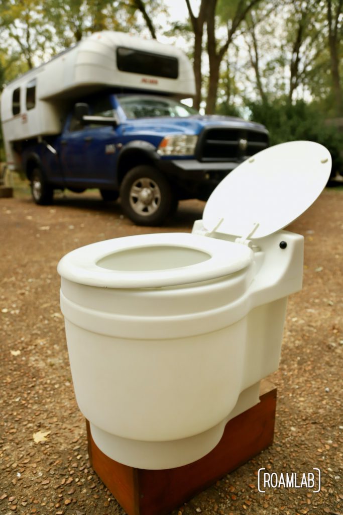 White dry-flush toilet with a 1970 Avion C11 truck camper on a blue Ram truck in the background.