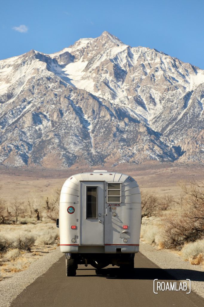 Rear view of a 1970 Avion C11 truck camper driving toward a snow capped mountain in the Sierra Nevada.