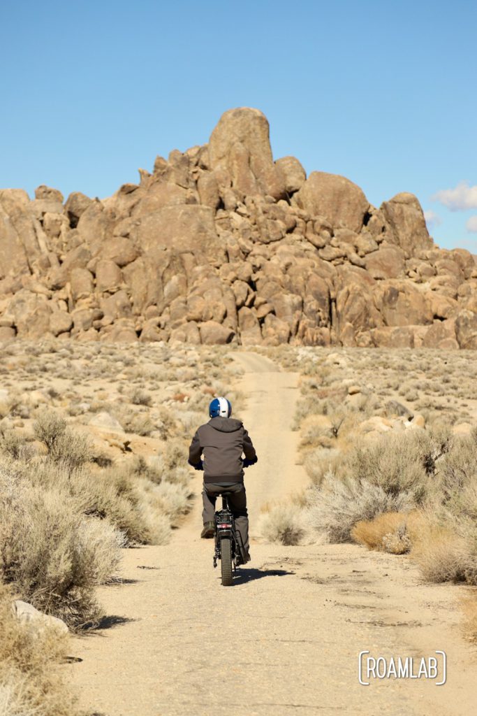 Man biking down a rough sandy trail toward a pile of boulders in the Alabama Hills.