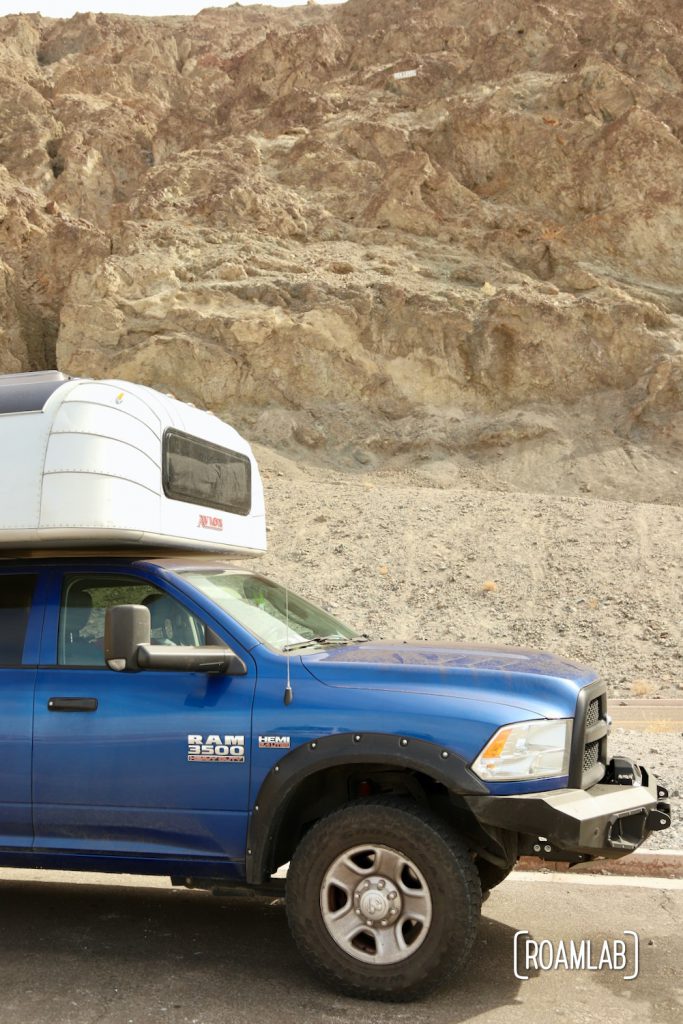 Blue truck and silver aluminum camper parked next to a tan cliff with a "sea level" marker hundreds of feet above