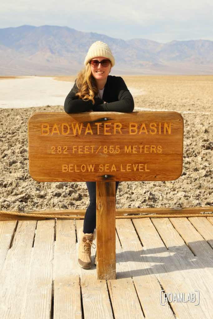 Woman standing behind sign for Badwater Basin.