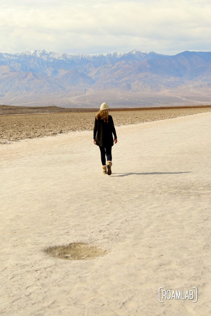 Woman in black walking out on a wide sandy trail of a dry lake bed in Death Valley's Badwater Basin.