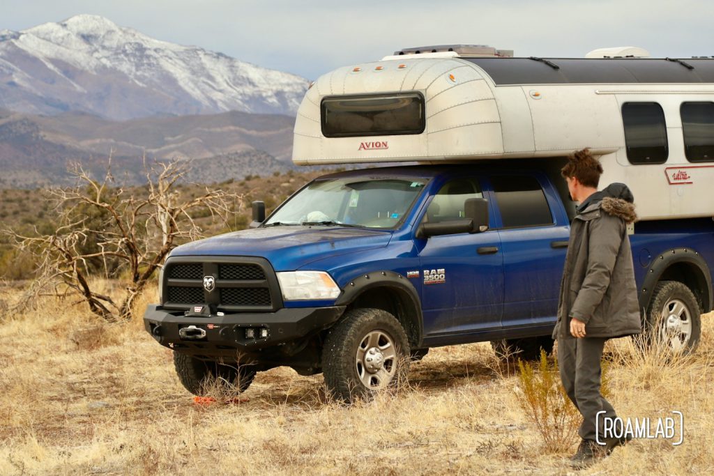 Man walking by a 1970 Avion C11 truck camper with a snow capped mountain in the distance from Lovell Canyon, Nevada