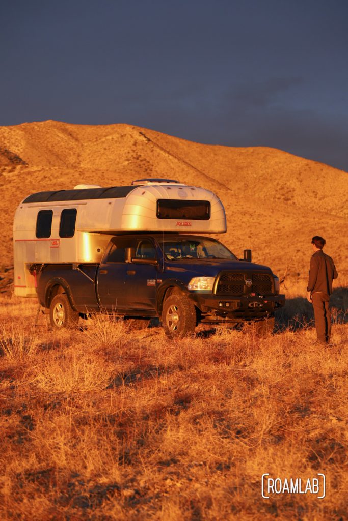 The golden rays of the sunrise casting the landscape and a 1970 Avion C11 truck camper and man in gold.