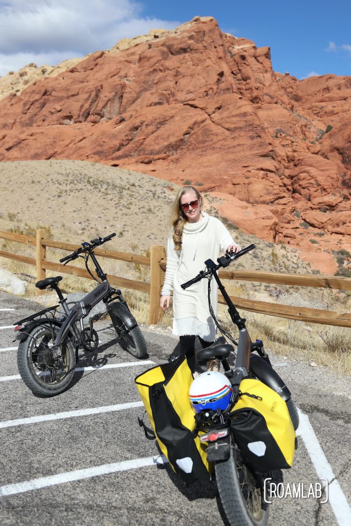 Woman standing next to her bike with a red cliff behind her.