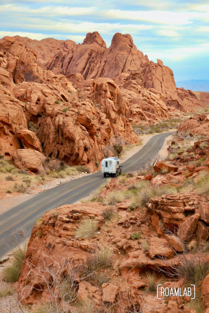 1970 Avion C11 truck camper flanked by red rocks driving down Mouse Tank Road in Valley of Fire State Park.