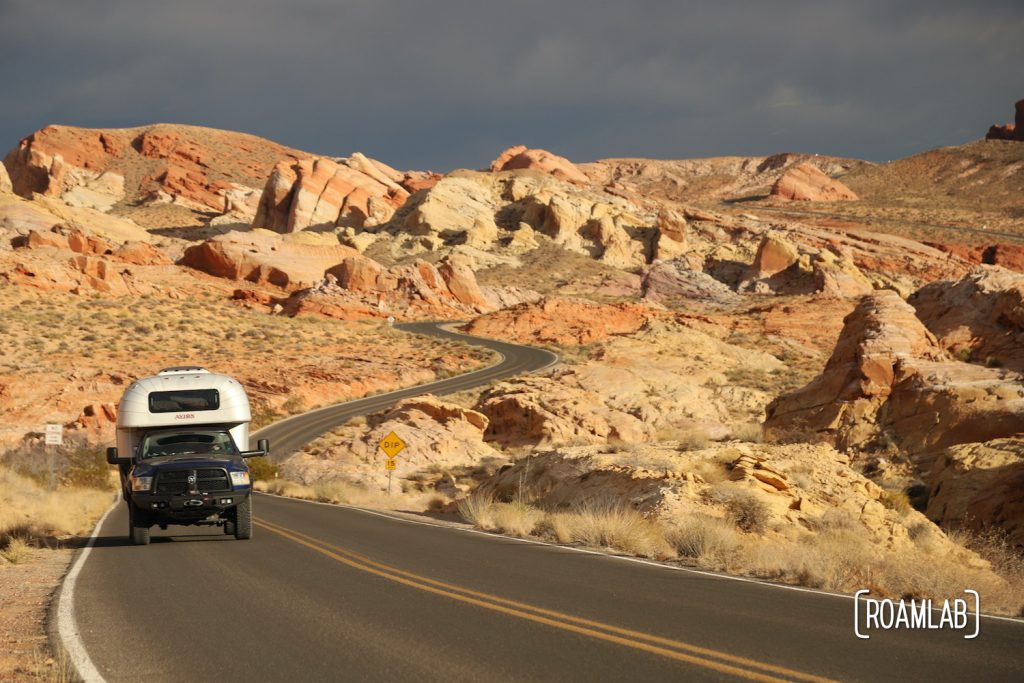 1970 Avion C11 truck camper driving through a rainbow of red rocks down Mouse Tank Road in Valley of Fire State Park.