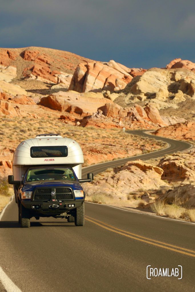 1970 Avion C11 truck camper driving through a rainbow of red rocks down Mouse Tank Road in Valley of Fire State Park.