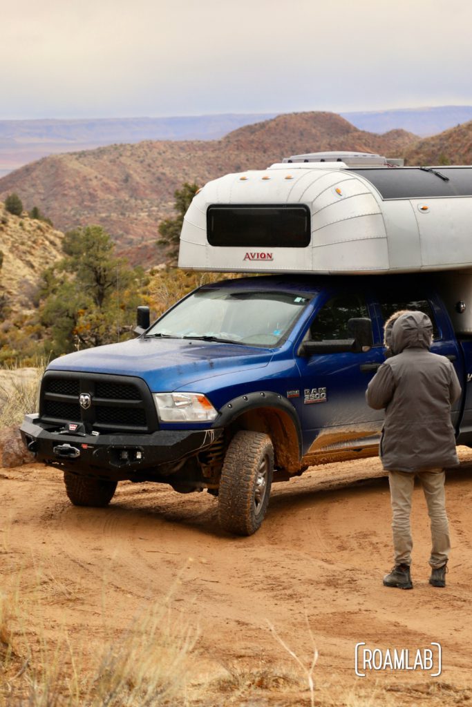 Man in large down coat in front of a 1970 Avion C11 truck camper with a mountain in the background of Dixie National Forest off Forest Road 031