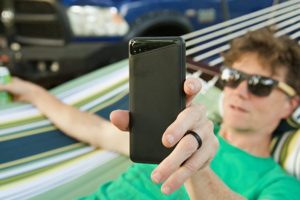 Man reclining in a hammock holding up a black GlocalMe TriForce wifi hotspot.