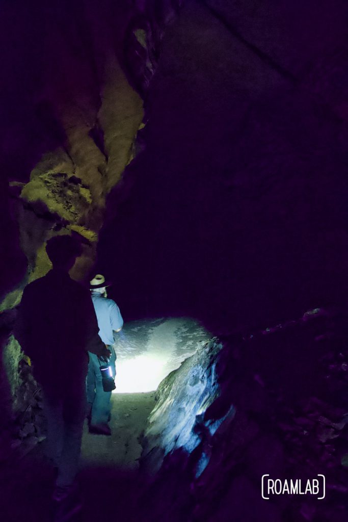 Man walking through a dark cave, faintly lit by lantern on the Geology Tour of Mammoth Cave National Park.